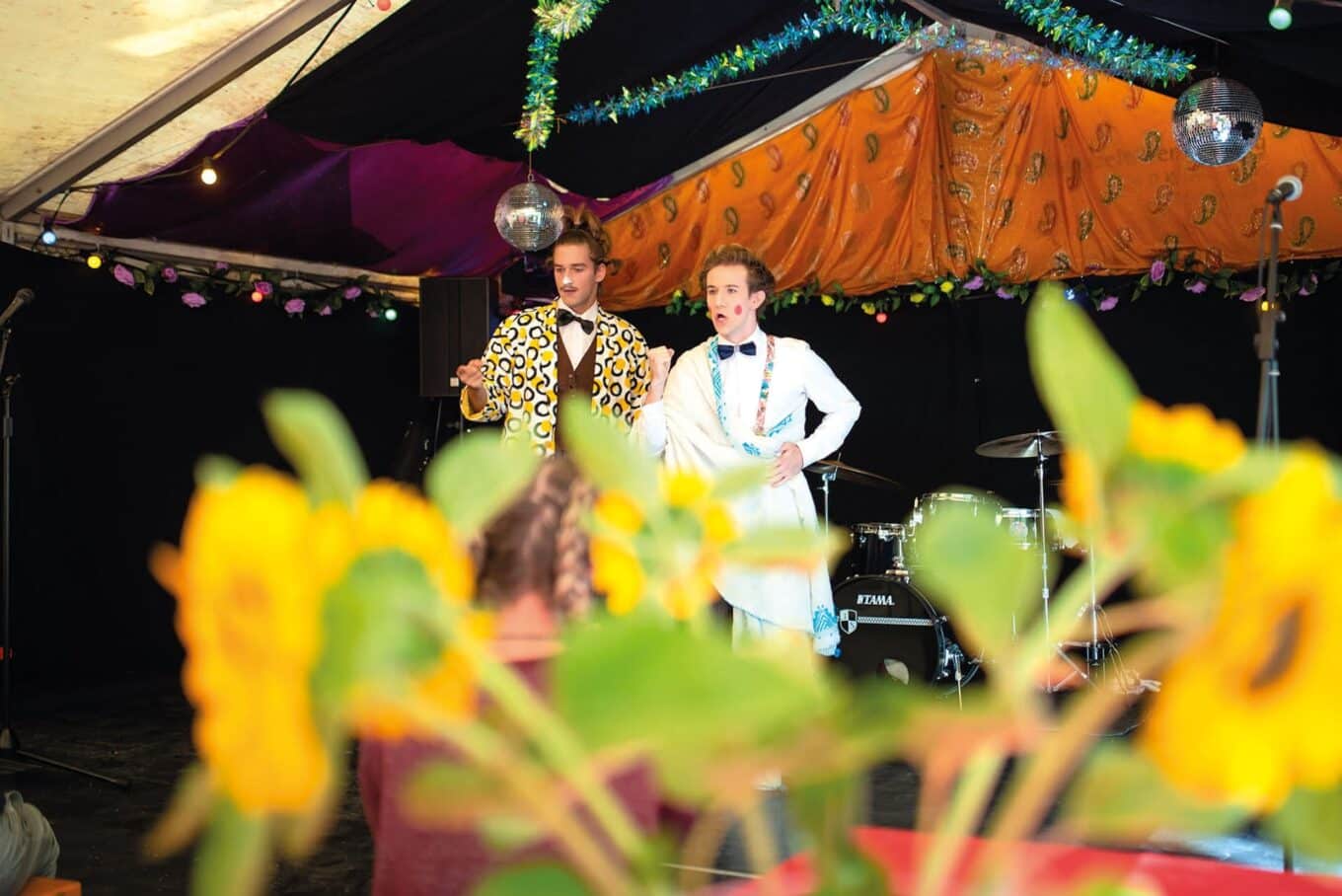 Zwei Clowns auf der Bühne, Sonnenblumen im Vordergrund.