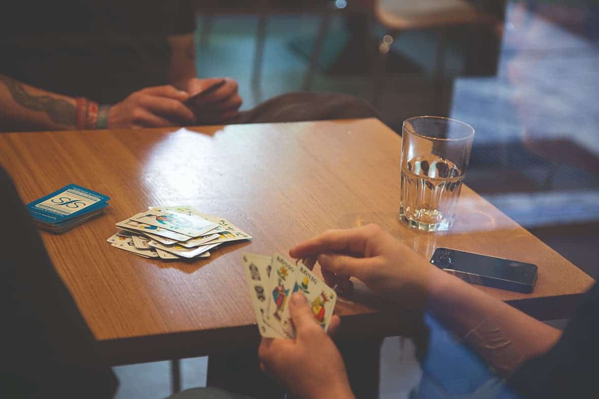 Personen spielen Kartenspiel am Holztisch mit Wasserglas