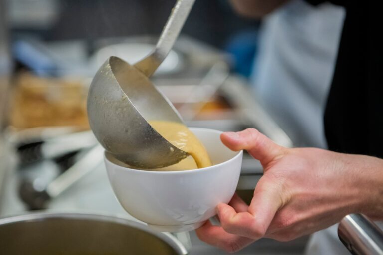 Koch serviert Suppe mit Schöpfkelle in weisse Schüssel