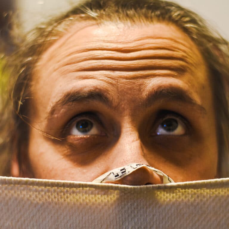 Person mit grossen Augen späht über Stoffrand hervor