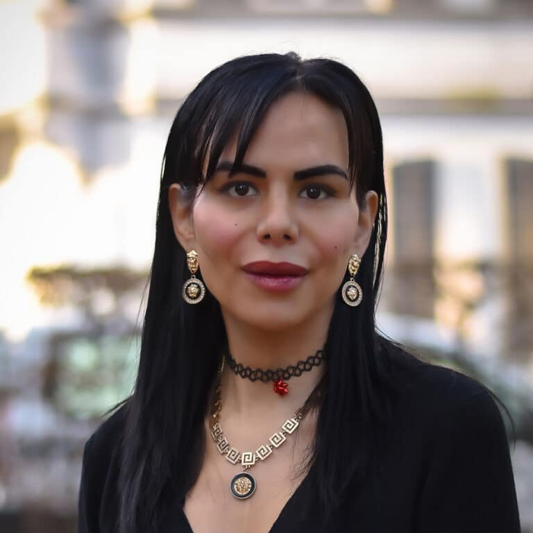 Frau mit schwarzen Haaren und goldenem Schmuck lächelt